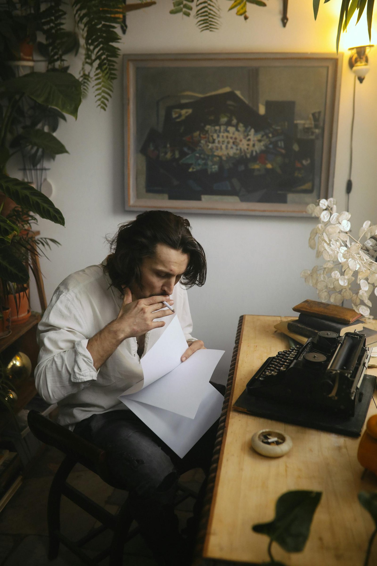 Man in casual attire smokes while examining papers at a rustic desk.